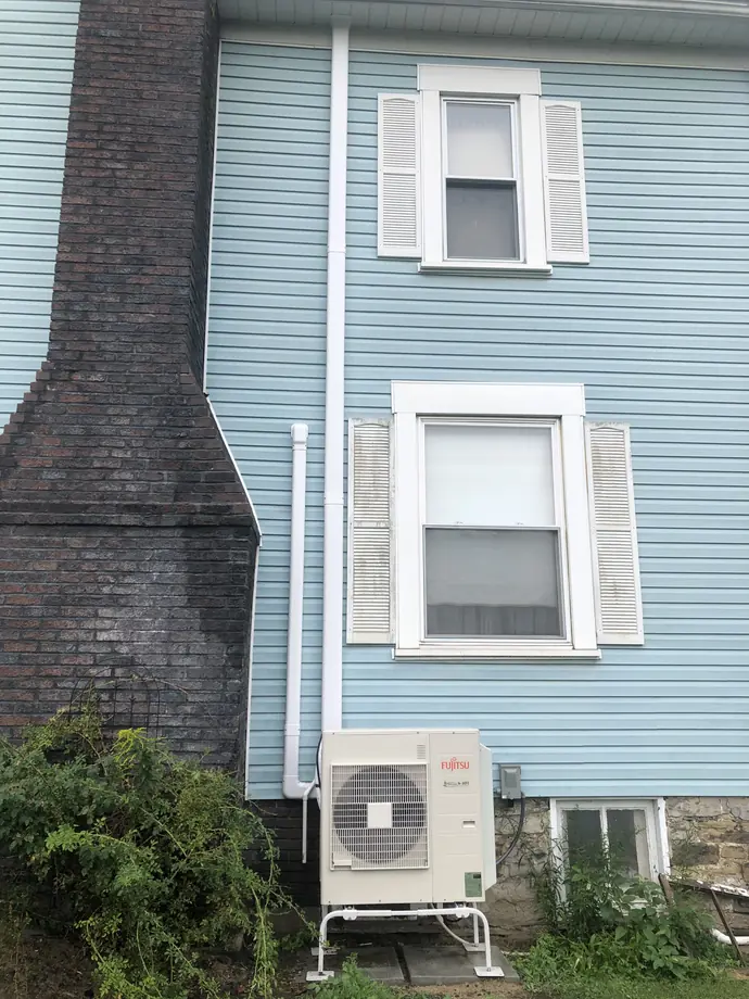 Ductless Fujitsu condenser with white line cover next to two-story blue residence