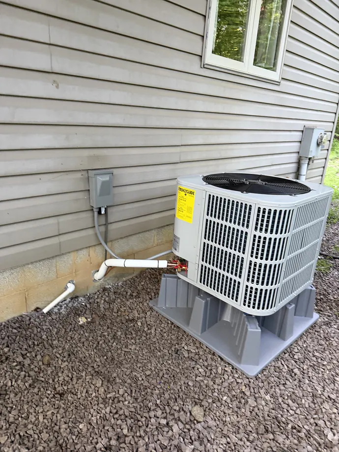 White outdoor HVAC unit installed beside gray siding and neat line routing