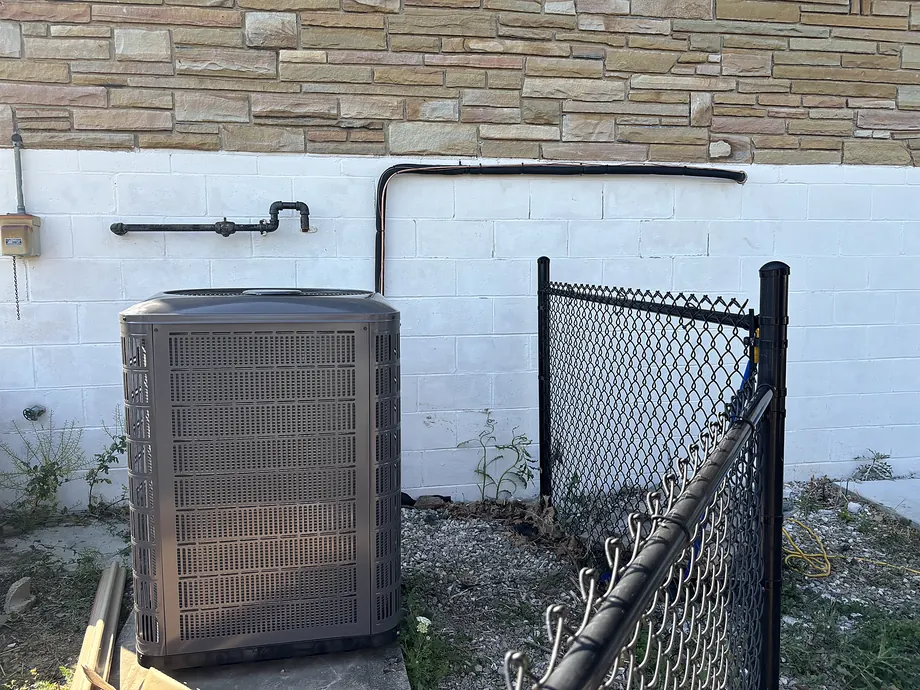 Outdoor HVAC condenser installed by white block wall