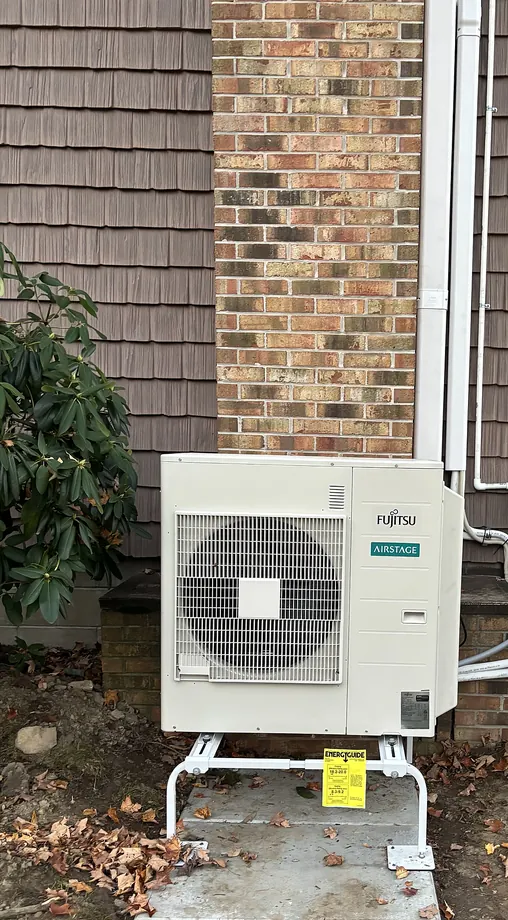 White Fujitsu ductless unit installed near brick wall with finished line covers