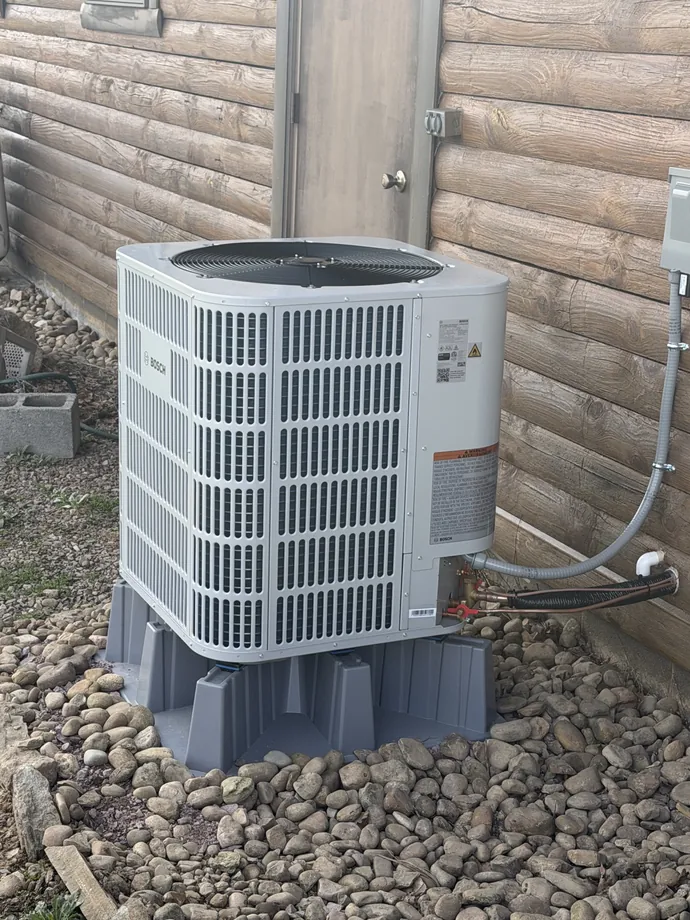 White Bosch condenser on a support stand beside timber siding and rock landscaping