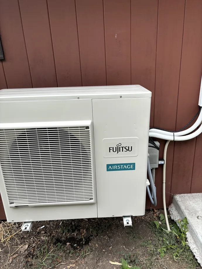 Fujitsu ductless outdoor heat pump with neat white line routing on a wood-sided home