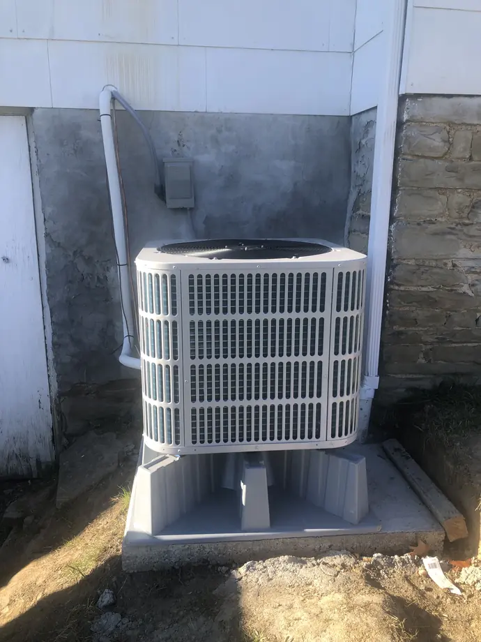 White condenser outside white-paneled residence above a foundation wall