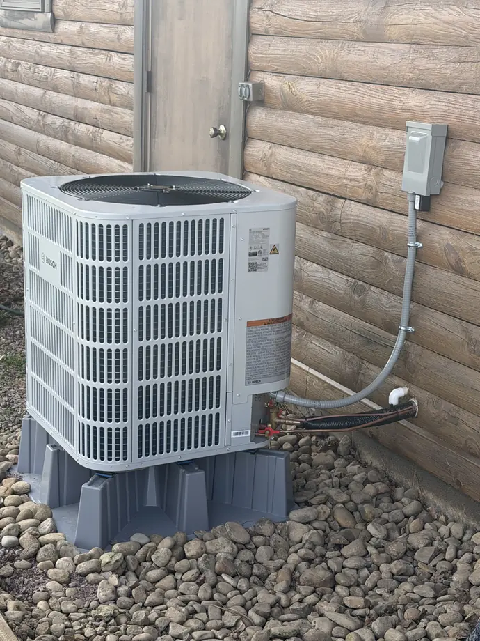 White Bosch outdoor condenser supported above river stone against timber siding