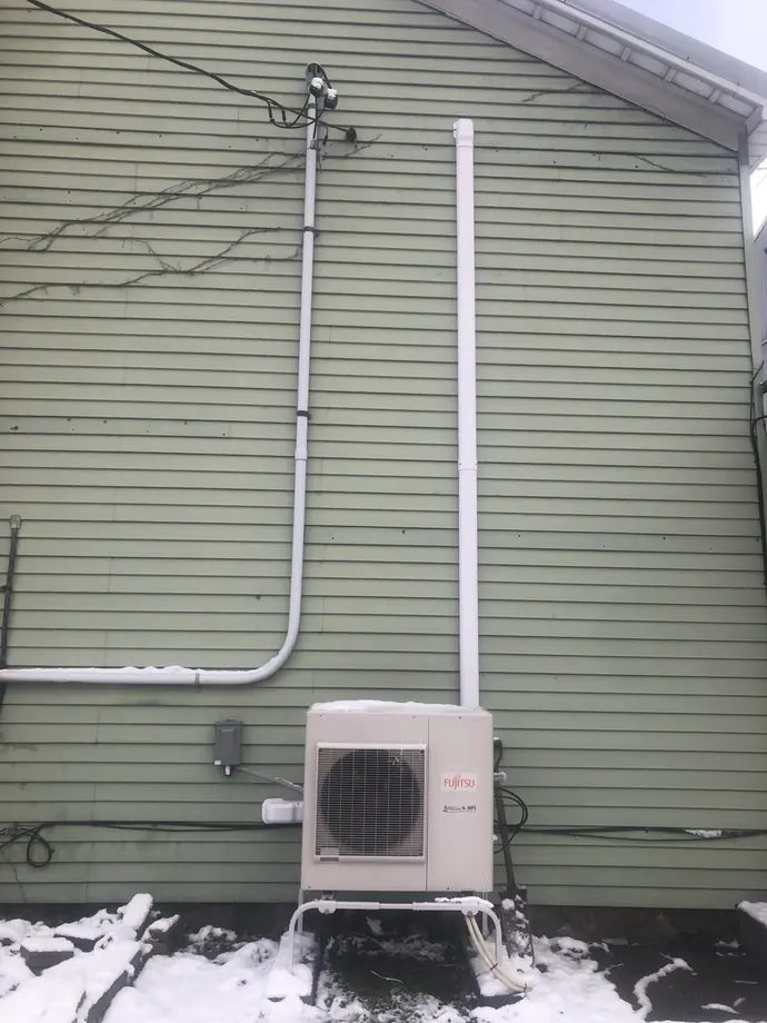 Installed Fujitsu ductless outdoor unit and white line covers beside house siding in winter